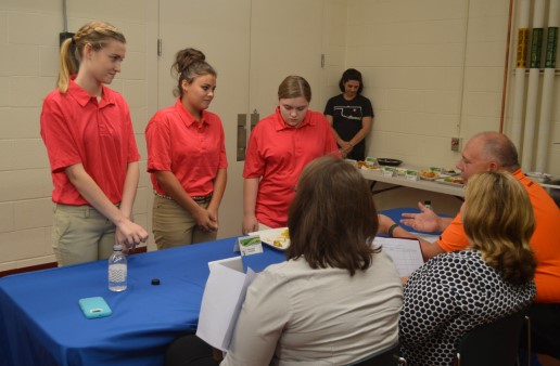 Three girls in orange shirts watching the judges judge their food for the contest.