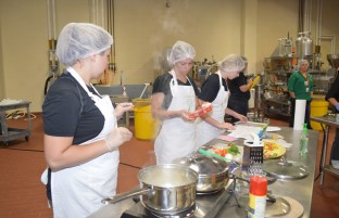 Three young girls in white aprons, cooking food together.