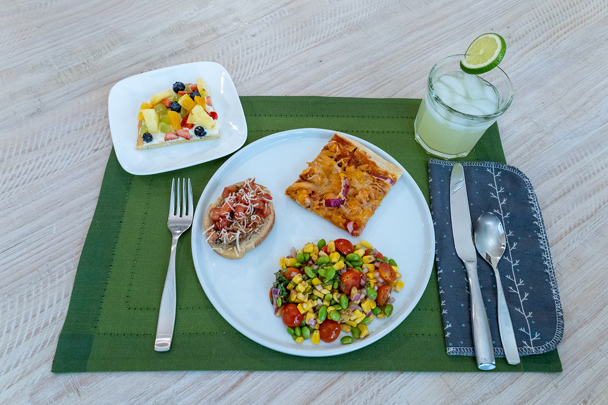 A plate on a table with chicken pizza, fruit, and a cinnamon roll