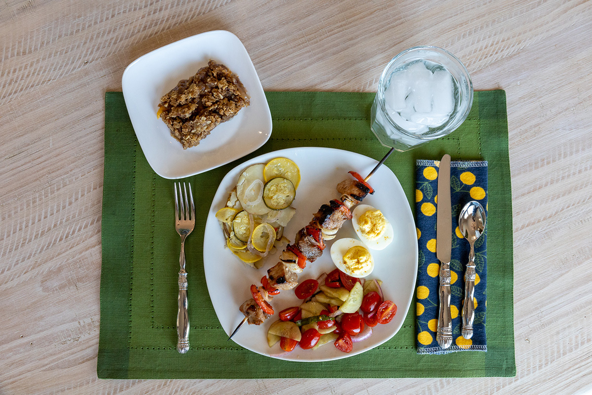 A plate on a table with pork kabobs, a tomato salad, and deviled-eggs