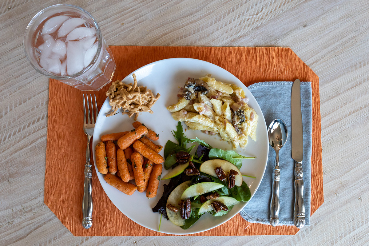 Pasta, carrots, a spinach salad, and cookies on a plate display